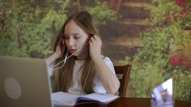 专注的年轻女孩戴着耳机，看着笔记本电脑视频下载