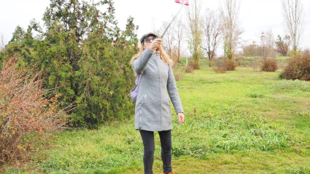 一个年轻的白人女孩在一个秋天的公园里散步，看着相机，微笑着用她的智能手机直播。通过直播的技术理念，生活方式。视频下载