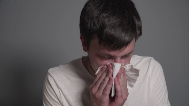 生病的年轻男子流鼻涕，患感冒或流感，坐在家里的床上打喷嚏。病毒或过敏。疾病。男性的病了。感染，流行病，细菌的载体视频素材