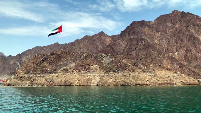 在蓝天白云的背景下，阿拉伯联合酋长国的国旗在哈塔湖中央的山顶飘扬视频素材