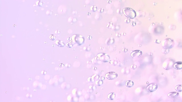 慢镜头和超微距镜头，在浅粉色和紫色的背景下倒水，产生微小的气泡视频素材