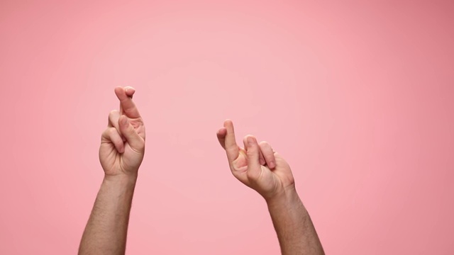 男人举起双手，交叉手指祈求好运，跳舞，在粉红色的背景上移动视频素材