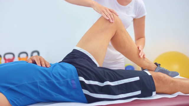 SLO MO女性运动按摩治疗师按摩男性运动员的膝盖视频下载
