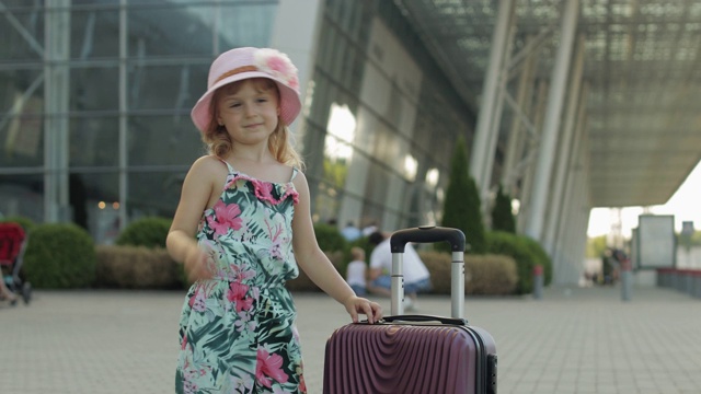 带着行李箱的女游客在机场附近。拿着行李的孩子跳舞，高兴，竖起大拇指视频素材