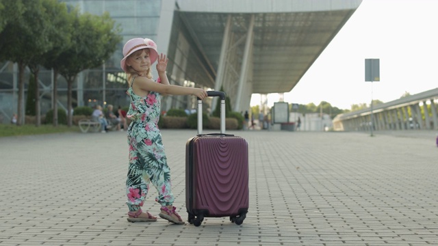 带着行李箱的女游客在机场附近。孩子挥手，拿着包走在街上。假期视频素材