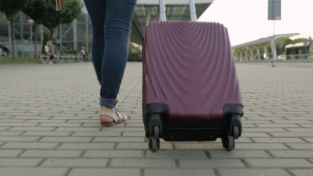 女商人带着行李走路的双腿。带着带轮子的旅行袋走在街上视频素材
