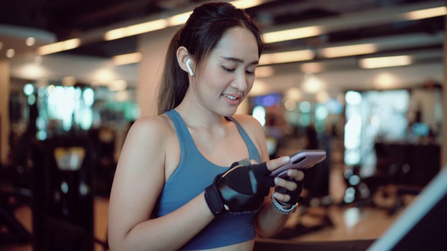 年轻的亚洲女性在健身房用智能手机听音乐视频素材