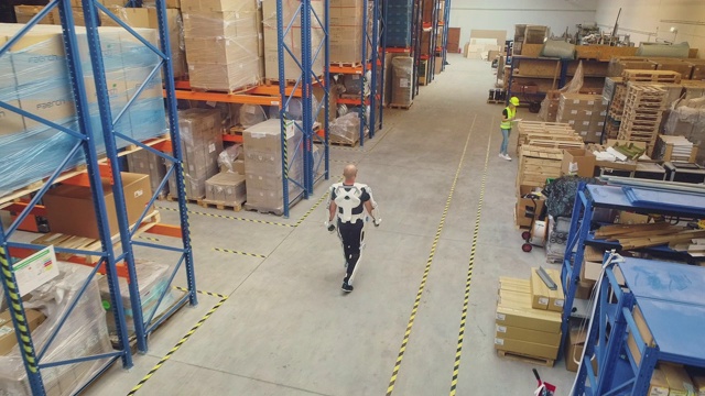 仓库工人穿着外骨骼在货架间行走。促进工作。鸟瞰图视频素材