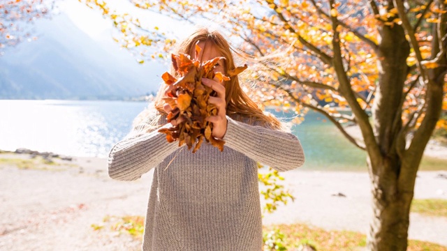 快乐的女人在湖边抛五颜六色的秋叶视频素材