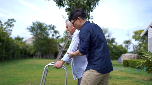 年长的亚洲人挣扎着给我们一个助行器。他已成年的儿子正在帮助他视频素材