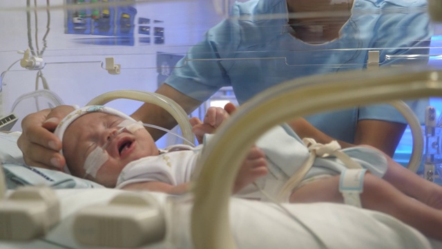 无法辨认的新生儿重症监护室护士试图安抚在保育箱里哭泣的婴儿视频素材