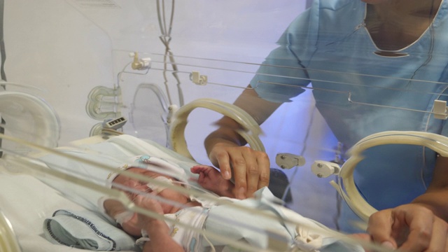 兴高采烈的新生儿重症监护室护士正亲切地安抚在保育箱里的婴儿视频素材