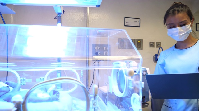 新生儿重症监护室年轻护士在检查孵化器新生儿病历视频素材