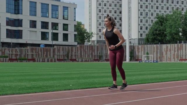 年轻的黑发女子在户外体育场做下蹲臀部运动视频下载