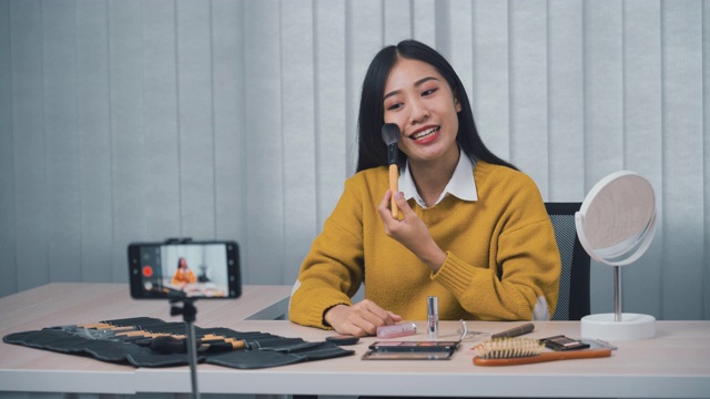 一位年轻的亚洲女性在家里用手机相机拍摄了一段关于化妆品的视频，并在她的博客上写了关于美容产品的视频。视频素材