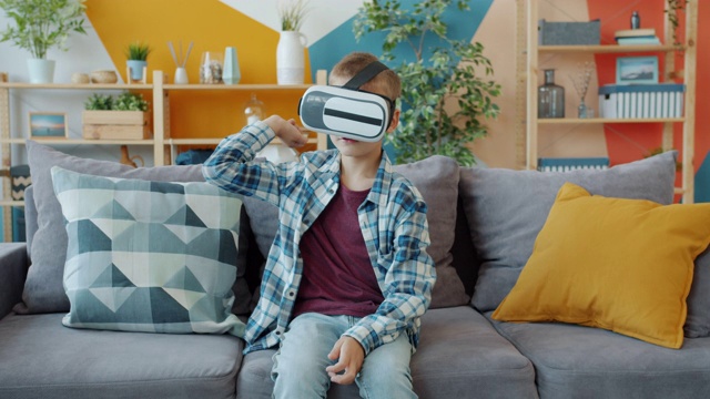 孩子享受虚拟现实眼镜坐在家里的沙发上手势放松视频素材