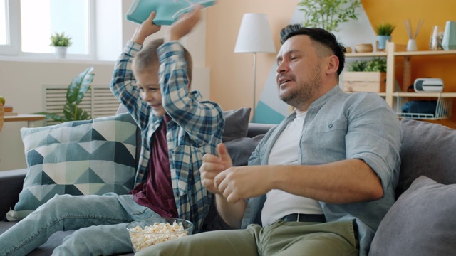 球迷爸爸和孩子在家里看电视比赛，手里拿着泡沫和球视频素材