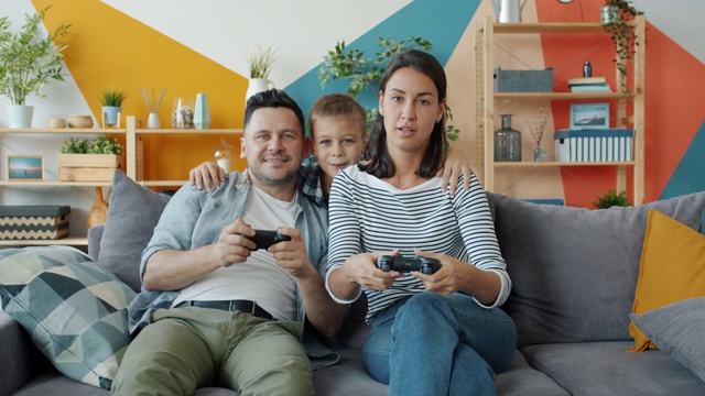 男人和女人在玩电子游戏，而快乐的孩子在家里拥抱父母视频素材