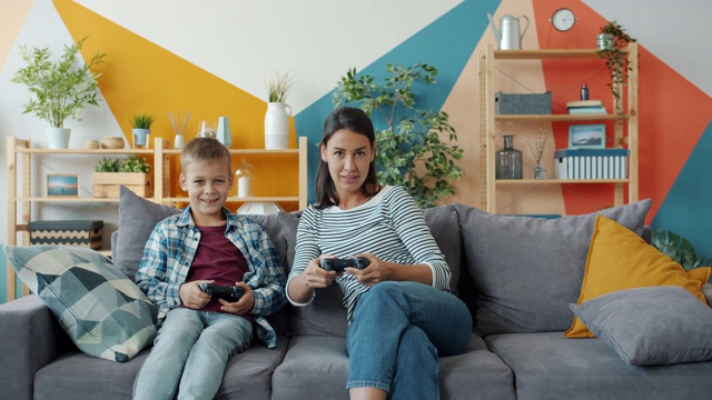 孩子在玩电子游戏，有爱心的妈妈拿着操纵杆在家说话视频素材