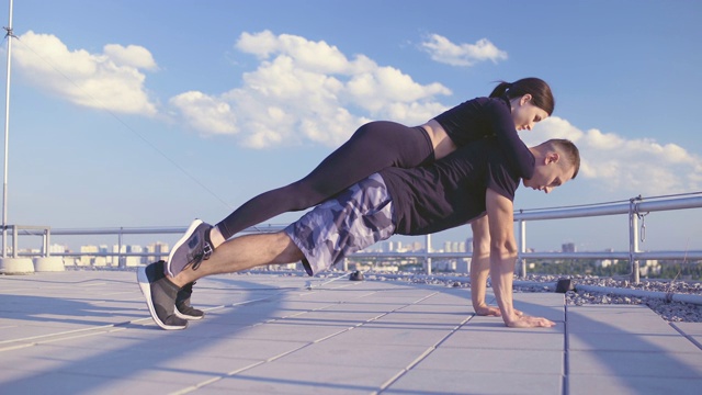 年轻的运动员和女友一起做俯卧撑，负重锻炼视频下载