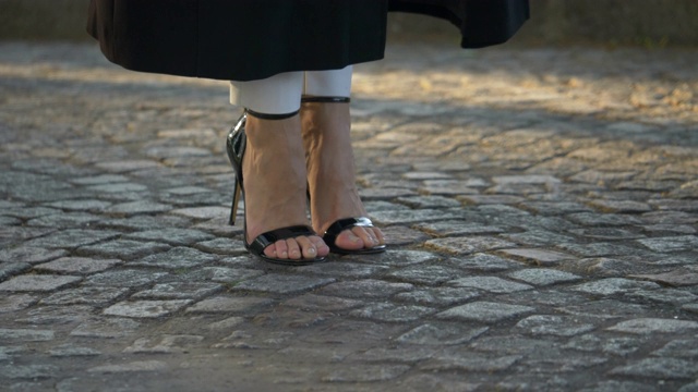 一个女人的脚在鹅卵石街道上穿着高跟鞋行走的特写细节。视频下载