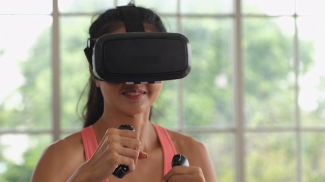 亚洲女性戴着虚拟现实耳机在家玩拳击运动的操纵杆。可穿戴技术视频素材