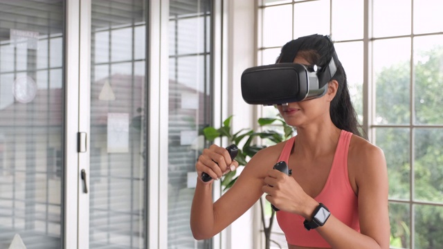 亚洲女性戴着虚拟现实耳机在家玩拳击运动的操纵杆。可穿戴技术视频素材