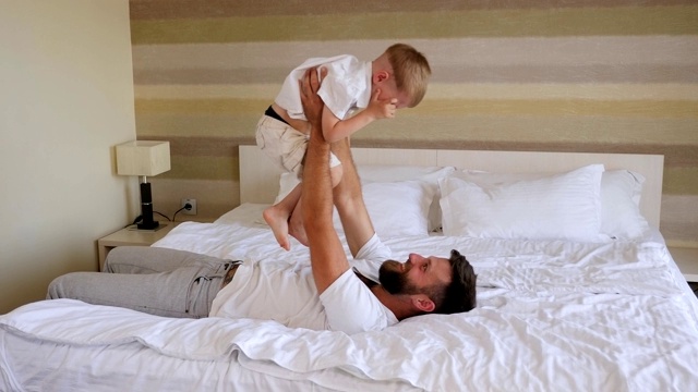一个快乐的父亲在酒店的床上和他的小儿子玩得很开心。视频素材