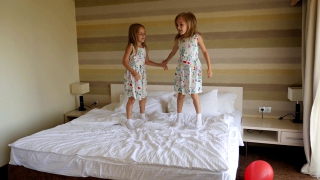 一对双胞胎姐妹早上在卧室的床上跳。视频素材