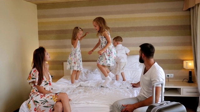 一家人正在酒店里放松，一个小儿子和一对双胞胎女孩在床上蹦蹦跳跳视频素材