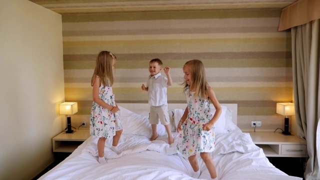 一对双胞胎女孩和一个小男孩在酒店房间的床上跳。视频素材