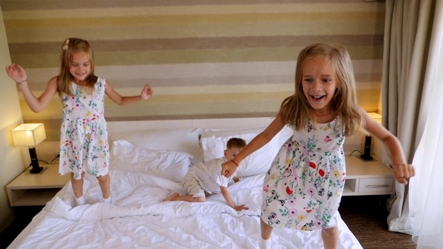 一对双胞胎女孩和一个小男孩在酒店房间的床上跳。视频素材