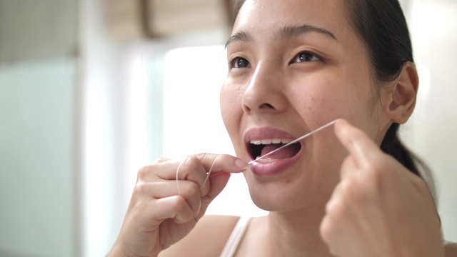 一个亚洲女人在家里的浴室里准备用牙线洁牙视频素材