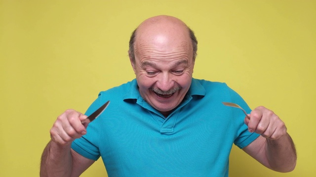 饥饿兴奋的西班牙老男人手里拿着刀叉准备吃。视频素材