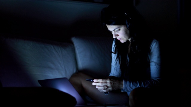 女人晚上使用手机和笔记本电脑，女孩深夜在屏幕前视频下载