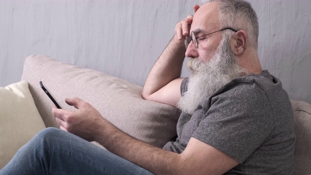 在沙发上玩智能手机的大胡子老人视频素材