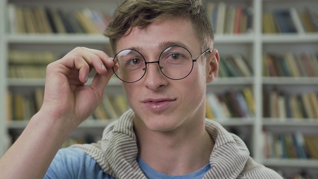 好看的整洁微笑的25岁男子在图书馆摆姿势的慢动作视频下载