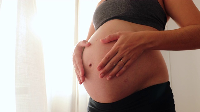 孕妇靠窗帘摸着肚子视频素材