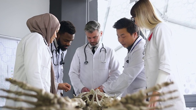 医学生和教授穿着医用服装，在医院灯光办公室的外科讲座上学习人体骨骼解剖学视频下载