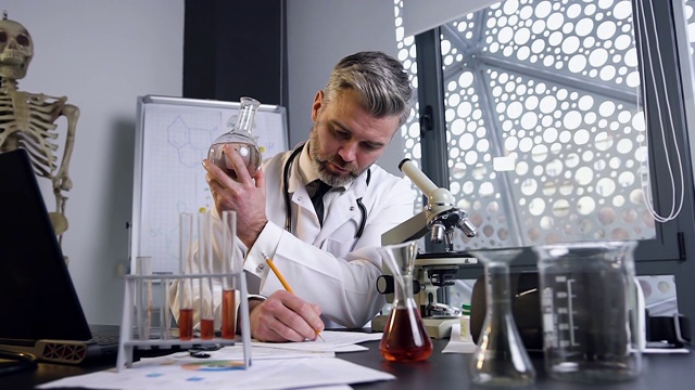 集中的中年科学家检查在实验室桌子旁的烧瓶中的化学液体视频素材