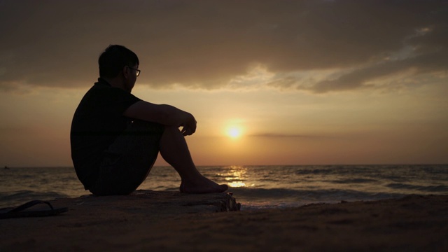亚洲男子沮丧和坐在海滩日落，芭堤雅视频下载