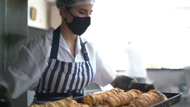女面包师用口罩从烤箱中取出新鲜面包视频下载