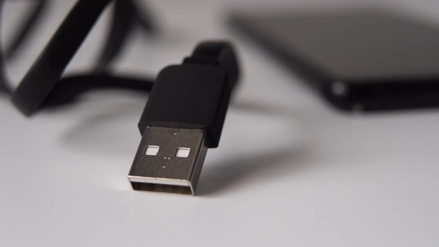 USB插头黑色与电缆放在白色的桌子上。模糊的黑色外置硬盘。视频下载