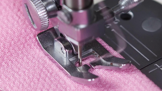 在缝纫机上缝制粉红色材料。缝纫机上移动的针的特写视频下载
