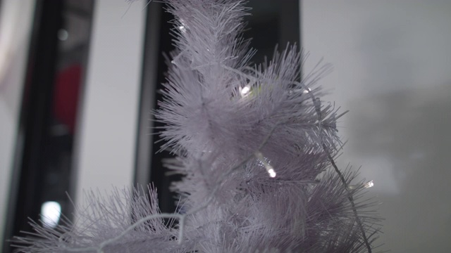 一双手把白色的灯挂在白色的圣诞树上，装饰着整个家。视频素材