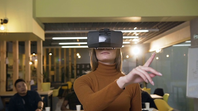 白种年轻女子戴着虚拟现实眼镜在办公室的空中滚动视频素材