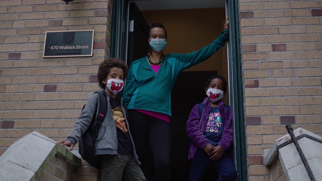 妈妈和两个孩子戴着医用口罩站在屋外视频下载