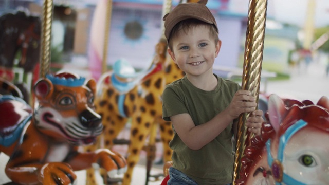 可爱的小男孩喜欢在游乐场玩旋转木马视频素材