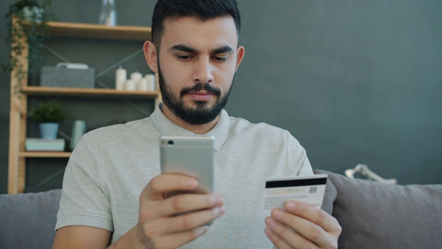 快乐的阿拉伯人在网上购物用银行卡和智能手机在家里付款视频素材