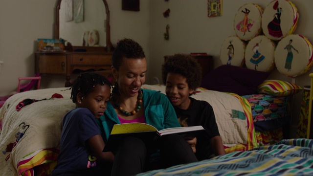 妈妈在家里的卧室里给儿子和女儿读书视频素材